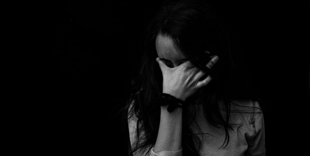 Black and white image of a woman with her hand to her forehead. She needs accessible and affordable mental health treatment.