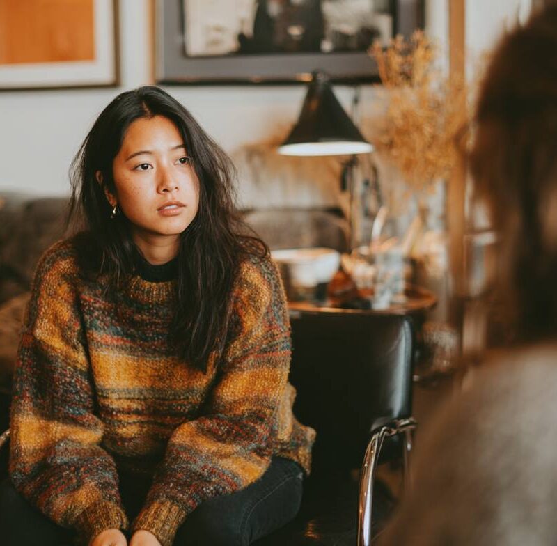 A young woman in a cozy sweater listens intently in therapy, reflecting how therapy for chronic stress and anxiety attacks can be accessed through Medi-cal.