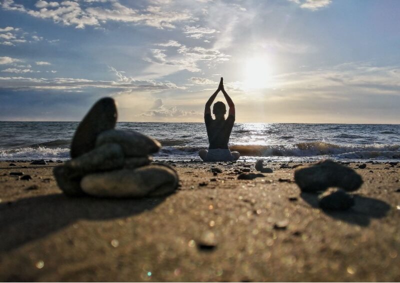 Person practicing meditation on a beach at sunrise to regulate your nervous system and reduce stress.